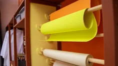 Rullar med färgglada papper hänger på rullar på väggen. Längre bort finns vita labbrockar på en stång.