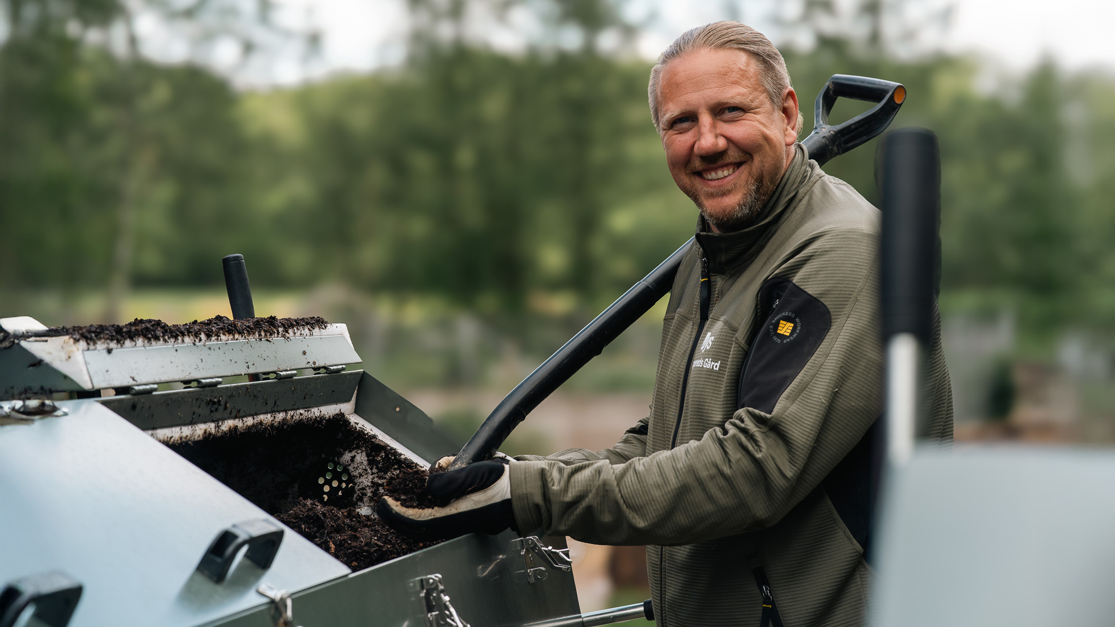 Tony står framför kompostbehållaren och håller kompostgödsel i handen