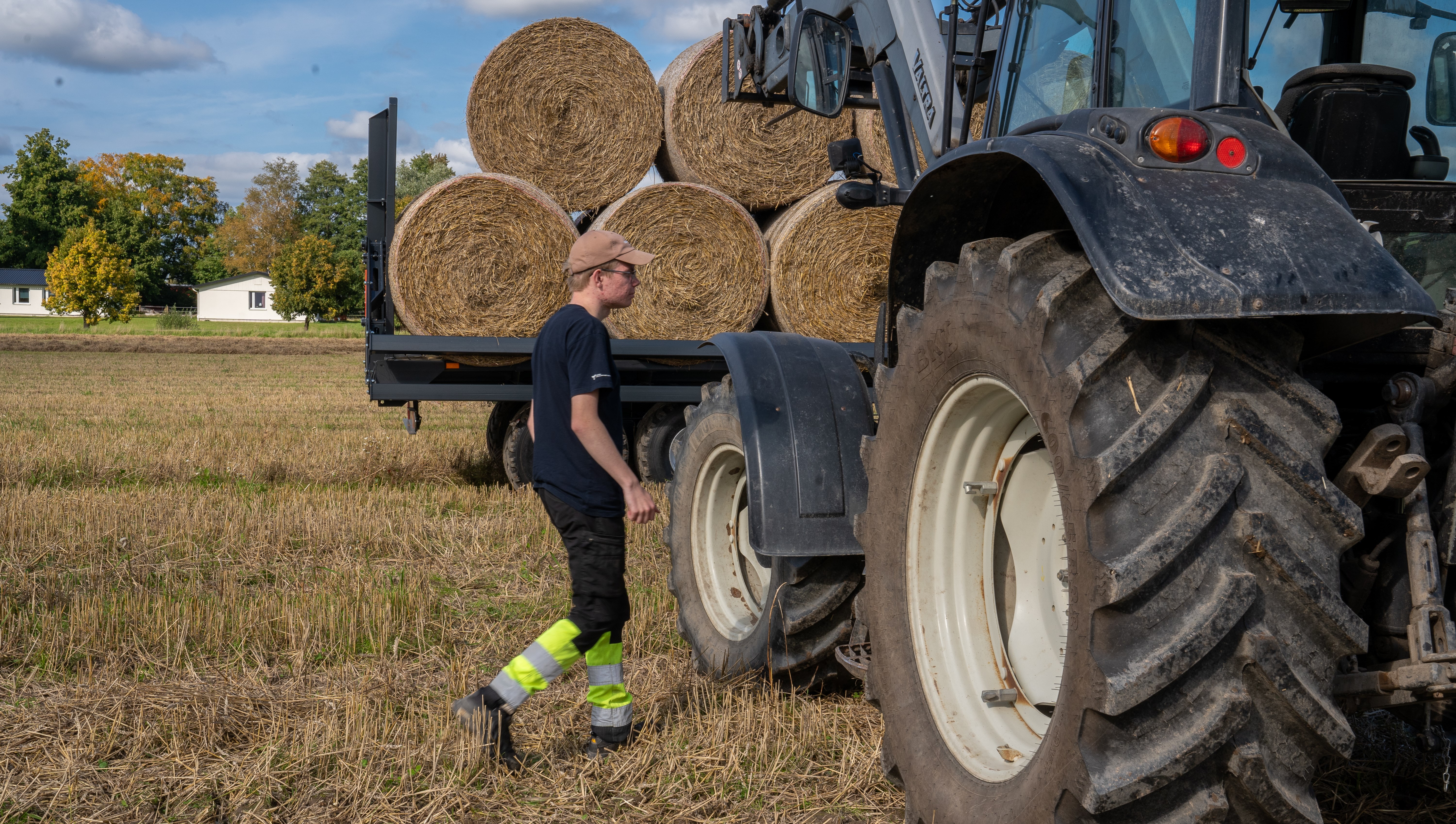Elev går mot traktor som står parkerad framför en balvagn på ett skördat fält