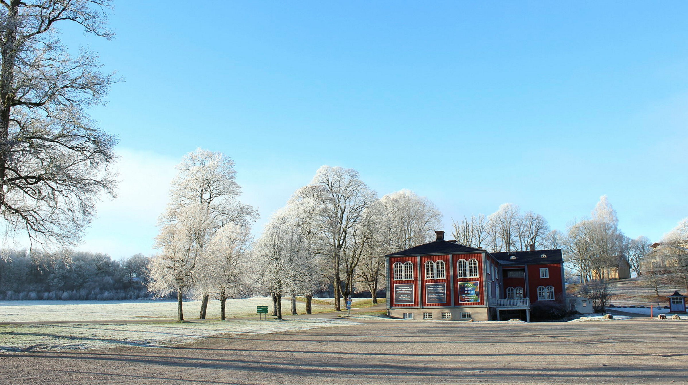 Ett rött hus vid en grusplan, blå himmel och frostiga träd