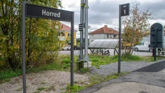 En skylt med texten Horred står på en tågperrong. bakom skylten finns ett par trähus och ett cykelställ.