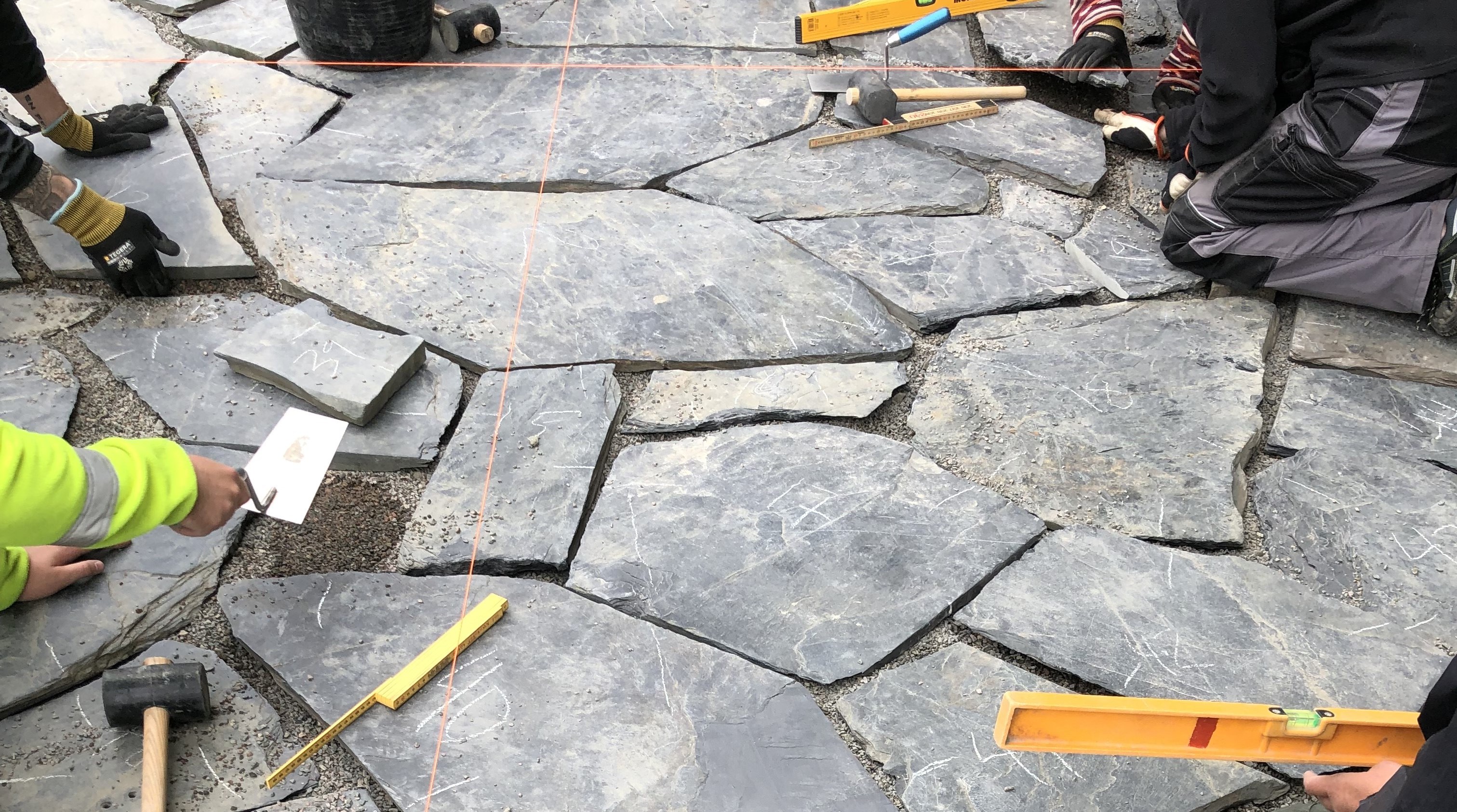 Händer jobbar med stensättning och olika verktyg