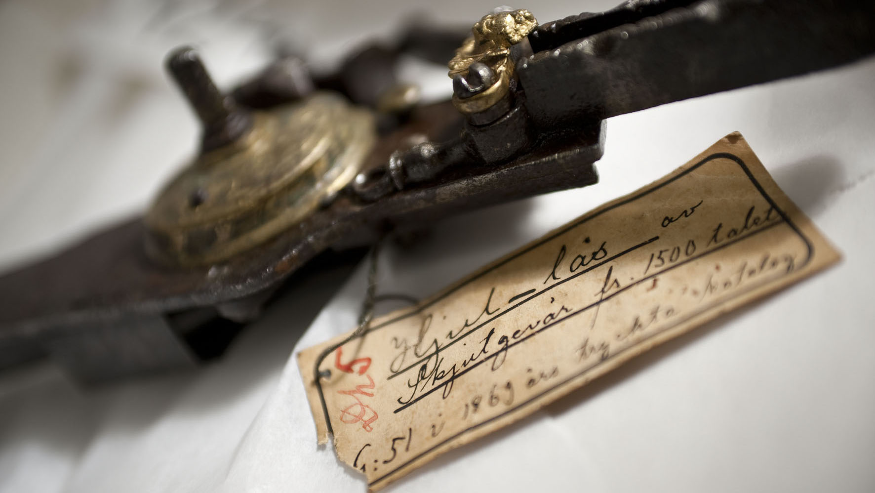 Ett äldre metallföremål med en gammal handskriven lapp fästad vid den.