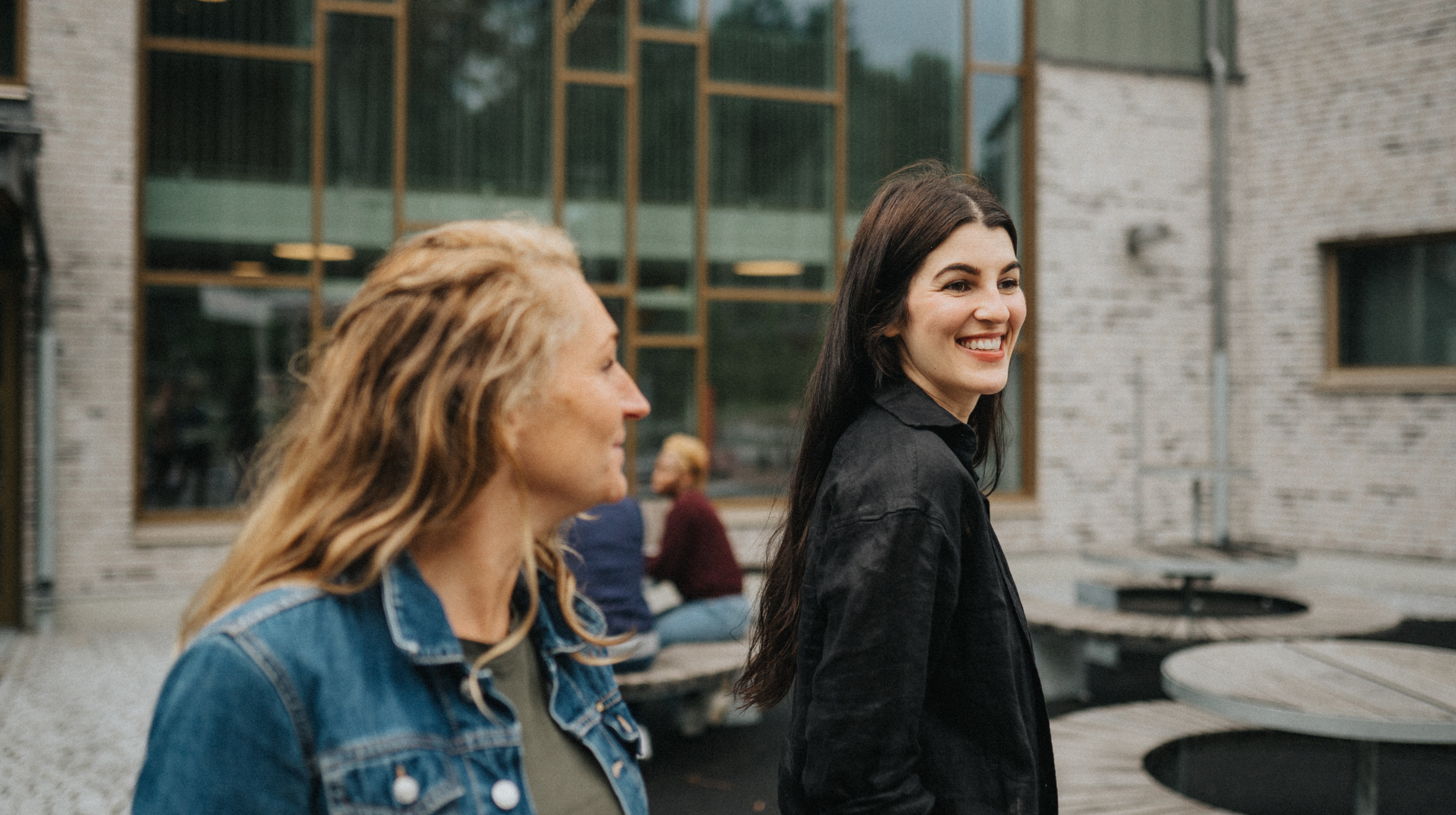 Två kvinnor samtalar vid en offentlig byggnad. Andra personer i bakgrunden vid en skola.