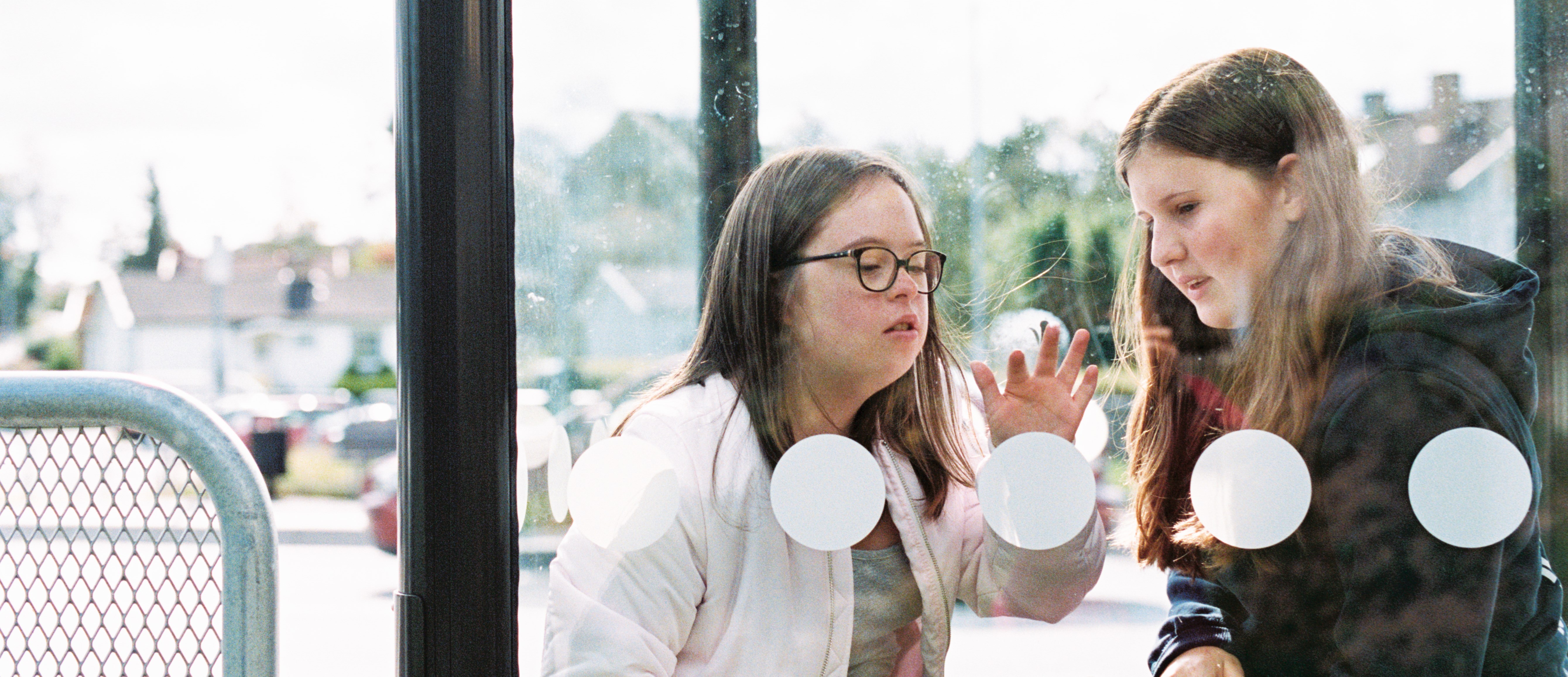 Fotografi taget framifrån. Två personer sitter i en busskur med glasväggar.