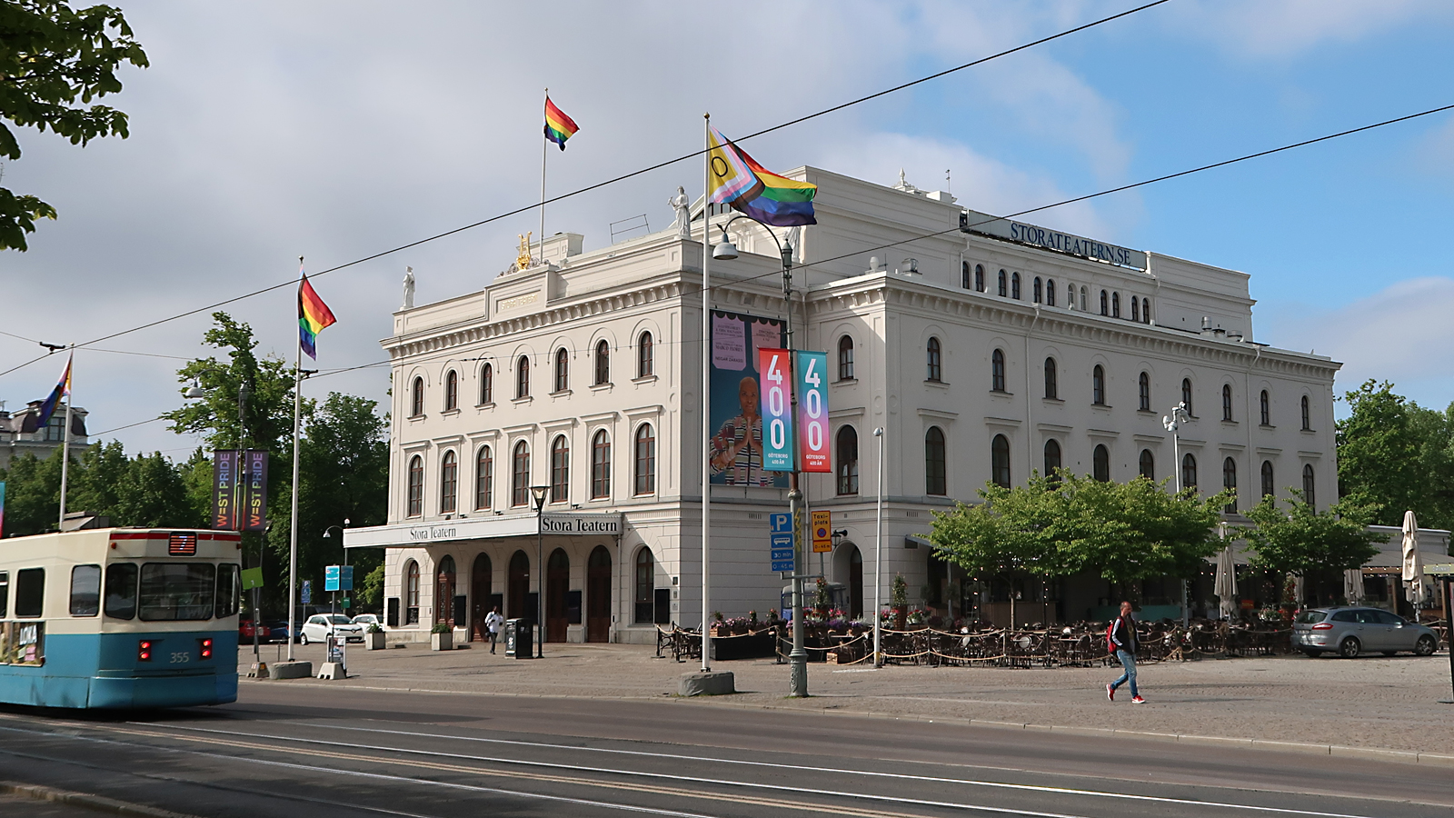 En gatuvy med ett stort vitt hus omgivet av grönskande träd.